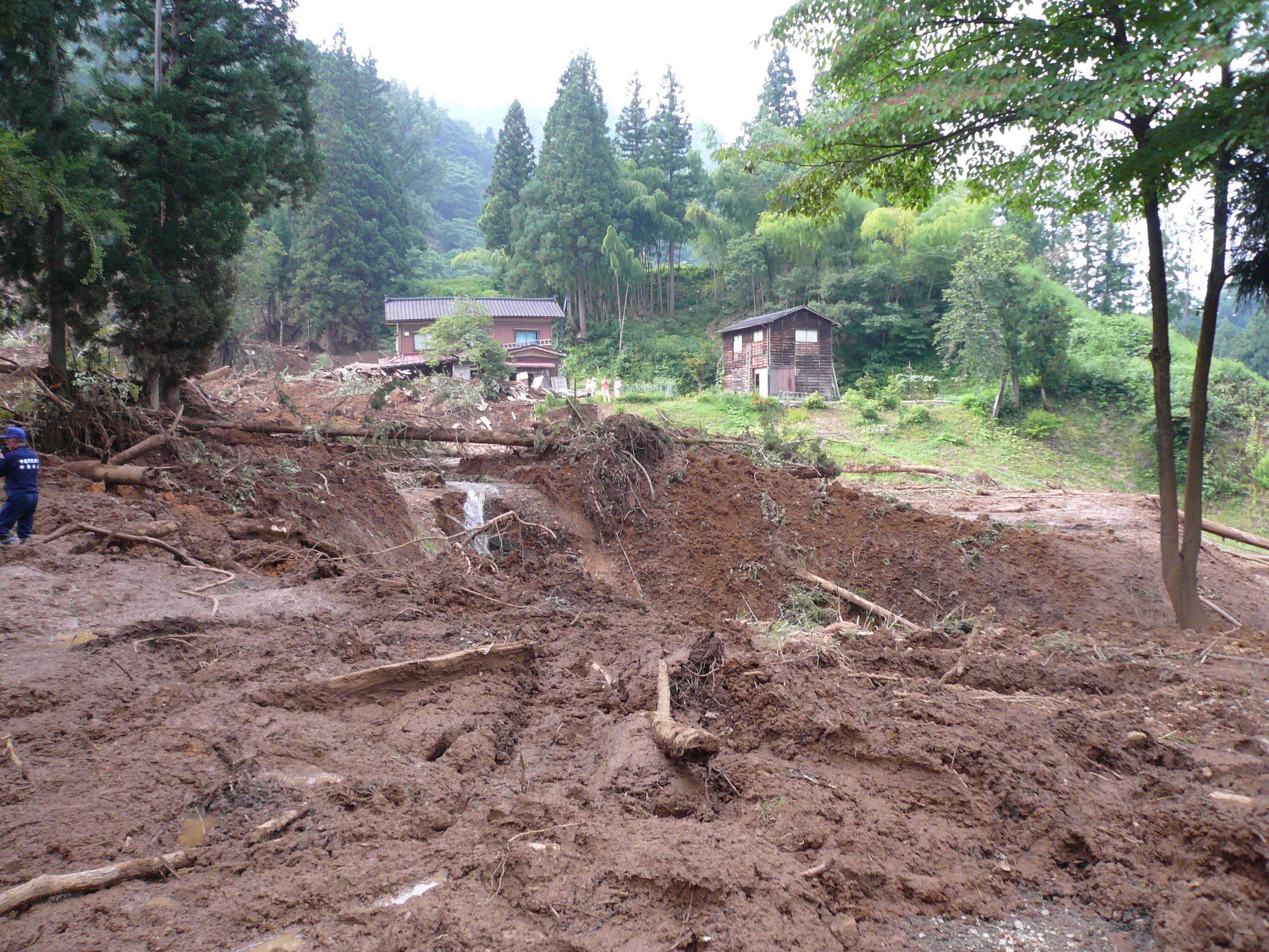 写真14 崩壊土砂の主体は地すべり地形の低い部分を流下したが,流動性が高かったため,やや高い位置にある住宅(写真奥)を巻き込んでいる.